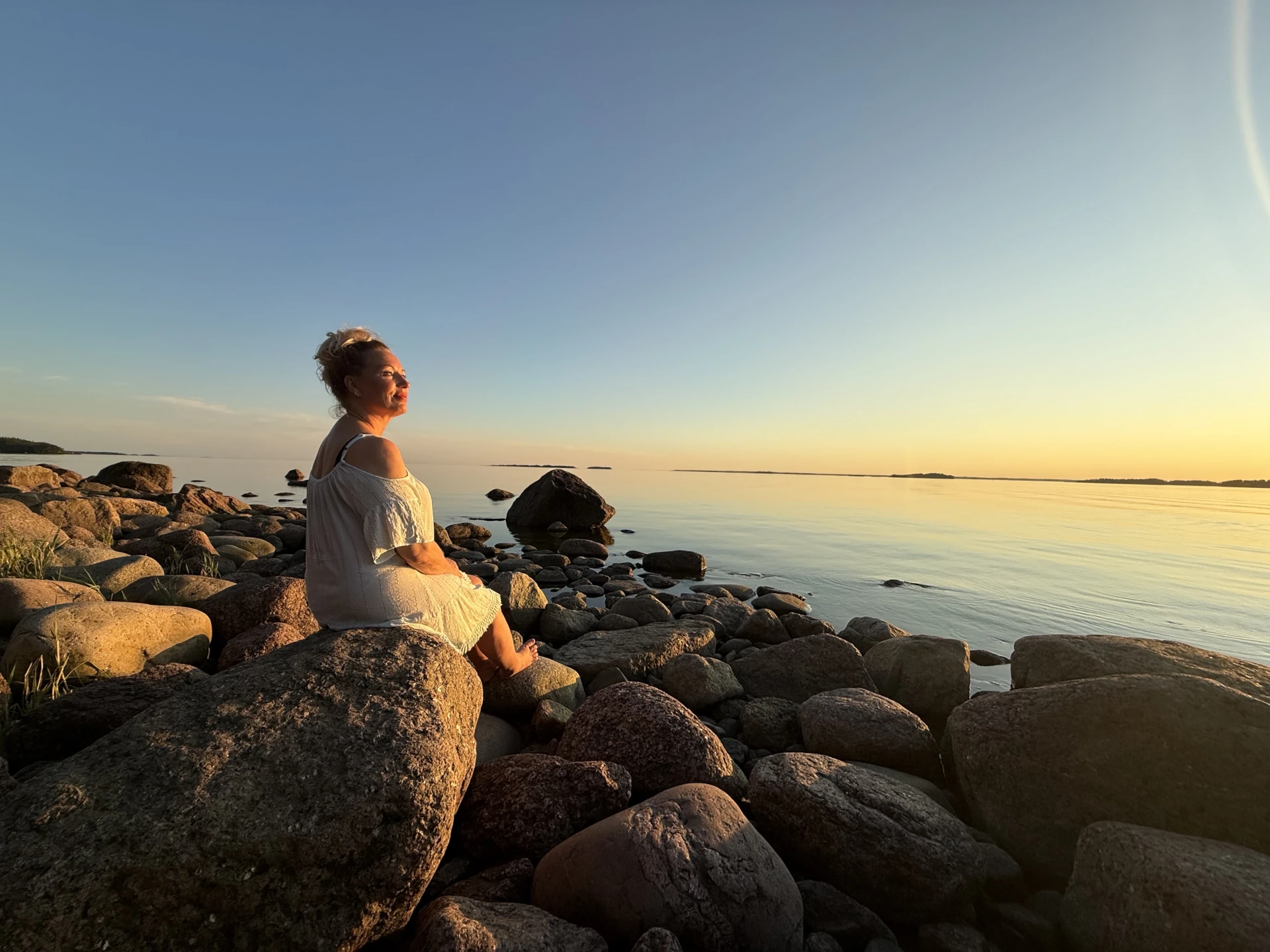 Inga istuu rantakivillä ja ihailee auringonlaskua